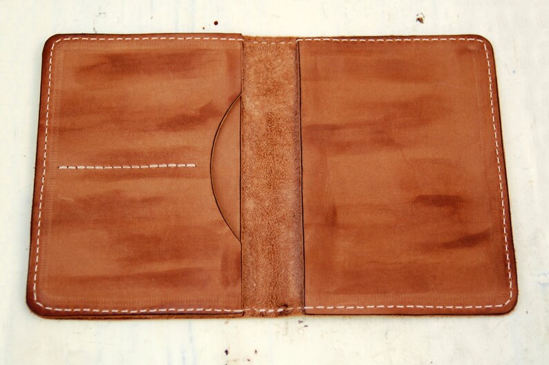 May include: A brown leather passport holder with white stitching. The holder has two pockets on the left side and one on the right.