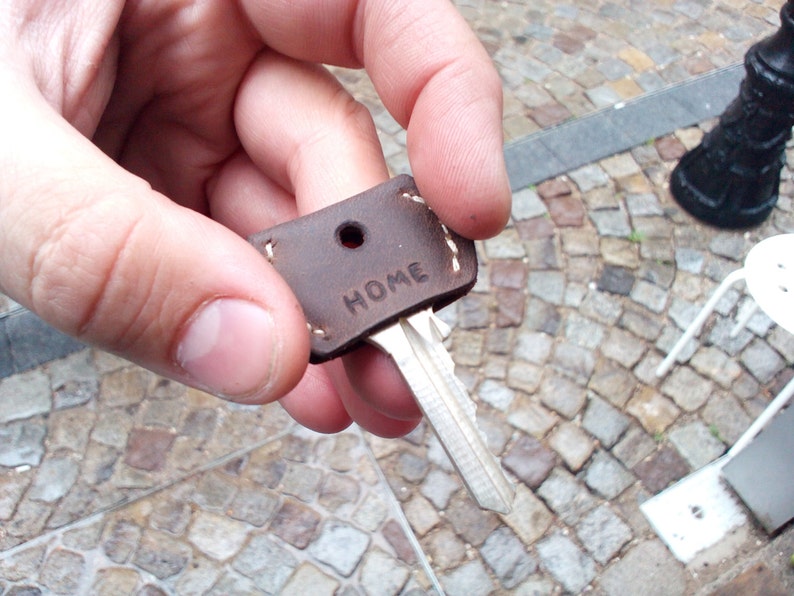 May include: A brown leather key fob with the word "HOME" embossed on it. The fob is attached to a silver key.