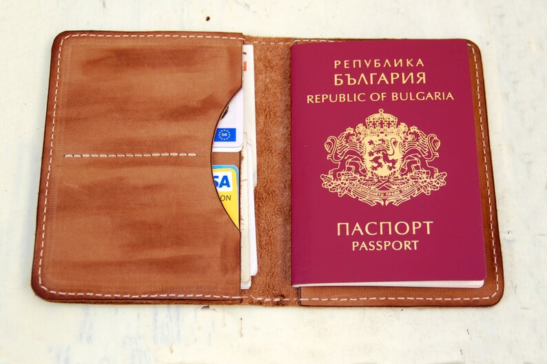 May include: A brown leather passport holder with a burgundy Bulgarian passport inside. The passport has the text "Република България" and "REPUBLIC OF BULGARIA" on the cover, along with the Bulgarian coat of arms. The passport holder has a pocket for cards and a flap to secure the passport.
