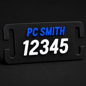 May include: A rectangular black identification tag featuring the blue text PC SMITH and the white numerical text 12345. The tag has rounded corners and vertical slots on both the left and right sides for attachment purposes.