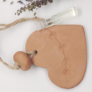 Peut inclure: Une décoration en forme de cœur en terre cuite avec une boucle en ficelle et une petite perle. La décoration a un motif floral délicat et est associée à un flacon en verre transparent d'huile essentielle.