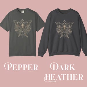 A pepper short-sleeved t-shirt and a dark heather long-sleeved sweatshirt, both printed with a gold and white moth design featuring crescent moons and floral details.