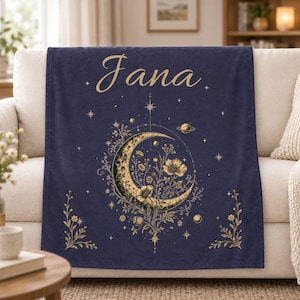 May include: A dark blue fleece blanket featuring the name Jana in gold script at the top. The center displays a gold crescent moon filled with floral illustrations, surrounded by small stars, planets, and delicate botanical sprigs.