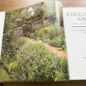 May include: An open book page displays a photograph of a lush garden with a brick path leading toward a house with a white gate. The text on the right page reads ENGLISH GA, FOR AME, TEXT AND PHO, FOR, and Incl.