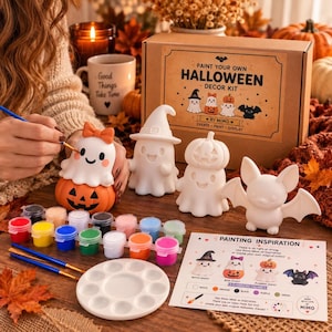 May include: A Paint Your Own Halloween Decor Kit by Mimo featuring a cardboard box, a white paint palette, two blue paintbrushes, twelve small paint pots, a painting inspiration guide, and four unpainted white ceramic figures: a ghost, a bat, and two ghosts with pumpkins.