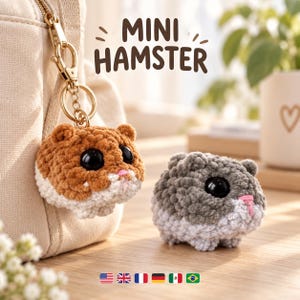 May include: Two crocheted hamster figures with large black eyes and pink noses. One brown and white hamster is attached to a gold-toned metal keychain, while a grey and white hamster sits nearby. The text MINI HAMSTER is visible above the figures.