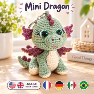 Puede incluir: Un llavero de dragón tejido a ganchillo en color verde con vientre crema, alas moradas y espinas dorsales moradas. El dragón tiene ojos negros grandes con pestañas largas, detalles de cuentas doradas en mejillas y alas, y una anilla metálica.