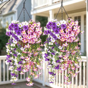 Peut inclure: Deux paniers suspendus remplis de fleurs artificielles aux couleurs vives. Les fleurs présentent un mélange de violet, de blanc et de rose, avec un feuillage vert retombant. Les paniers sont suspendus par des chaînes noires, créant un affichage coloré.