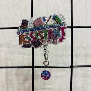 May include: A glittery acrylic badge reel featuring the text Administrative Assistant in colorful, patterned block letters. The design includes illustrations of office supplies like a calculator, glasses, and pens, with a circular purple glitter accent.