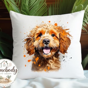 May include: White square throw pillow featuring a watercolor-style portrait of a happy, light brown dog with orange and black paint splatters. The dog has a pink tongue and is smiling. The pillow has a Homebody Gift Shop logo.