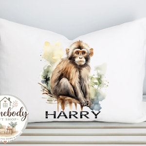 May include: White decorative pillow featuring a watercolor illustration of a monkey. The monkey is brown and tan, perched on a branch, with the name "HARRY" printed below. The pillow has a Homebody Gift Shop logo in the lower left corner.