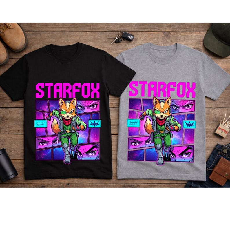 May include: A black t-shirt and a gray t-shirt, each featuring a graphic print of the character Fox McCloud from Starfox. The design includes the text STARFOX in bright pink, a space-themed background with comic-style panels, and a green visor.
