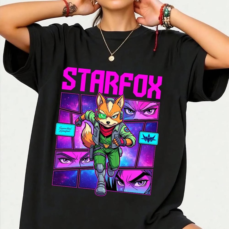 May include: A black short-sleeved t-shirt featuring a graphic print with the text STARFOX in bright pink. The design includes a central illustration of a fox character in a green flight suit, surrounded by comic-style panels with space imagery.
