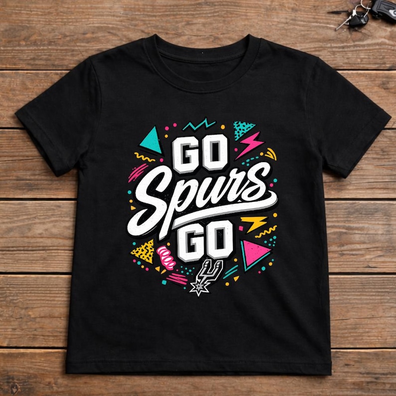 May include: Black t-shirt with the words "GO Spurs GO" in white, with colorful geometric shapes and the Spurs logo. The design has a retro 80s and 90s style.