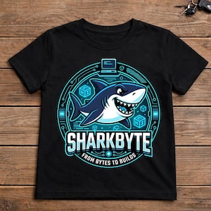 Op de afbeelding: Een zwart t-shirt met een cirkelvormige afbeelding van een cartoonhaai omringd door digitale circuitpatronen, kubussen en een computerpictogram. De tekst SHARKBYTE en FROM BYTES TO BUILDS is in wit en lichtblauw in het ontwerp gedrukt.