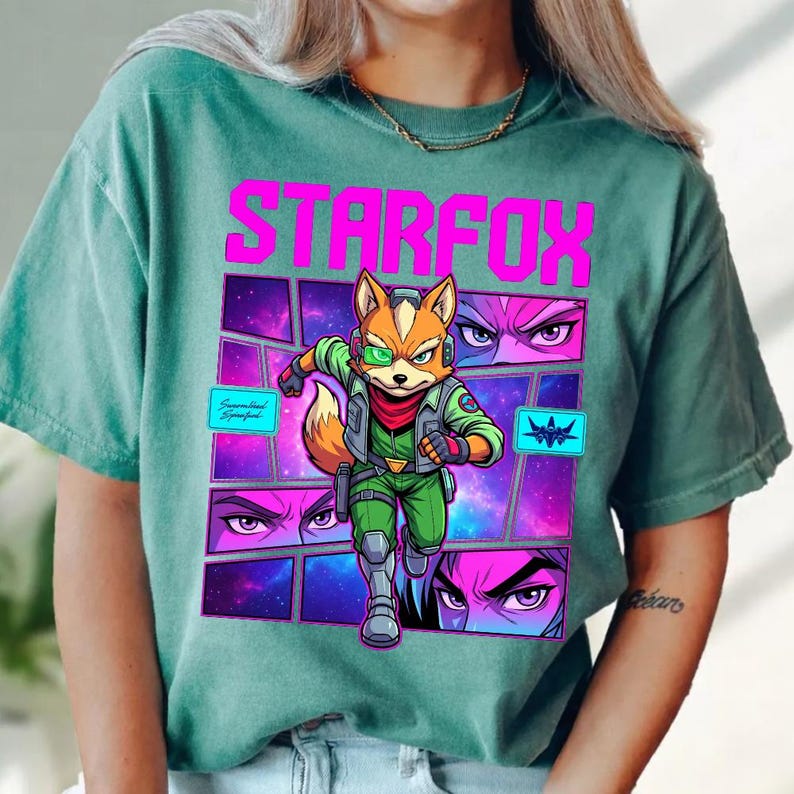 May include: A faded teal t-shirt featuring a graphic print of the character Fox McCloud from Star Fox. The design includes the text STARFOX in bold pink letters, a space-themed background, and close-up panels of character eyes in purple.