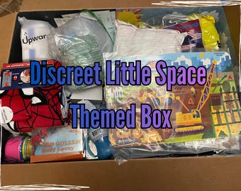 May include: A cardboard box filled with various items, including a Spider-Man blanket, a construction-themed puzzle, and a baby bottle. The box is labeled "Discreet Little Space Themed Box" in blue and purple text.