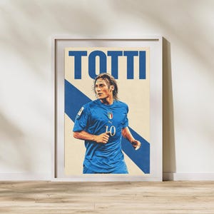 以下が含まれることがあります： 背番号10の青いユニフォームとイタリア代表チームのエンブレムを身に着けたサッカー選手のグラフィックイラストが描かれた、額縁入りの縦型ポスター。ポスターの上部には、青い大きな大文字でTOTTIと印刷されています。