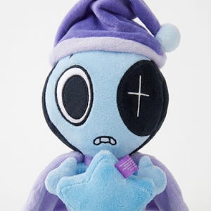 May include: A plush toy alien with a light blue face, large white-rimmed eyes, and a black patch over one eye. It wears a purple nightcap and holds a blue star. The toy has a stitched mouth and a purple cape.
