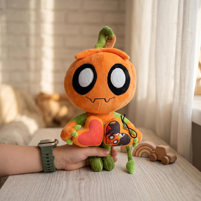 May include: An orange plush pumpkin character with large black and white eyes, a stitched mouth, and green arms and legs. It holds a red heart and a small pouch with a spooky design. The plush toy is designed for Halloween.