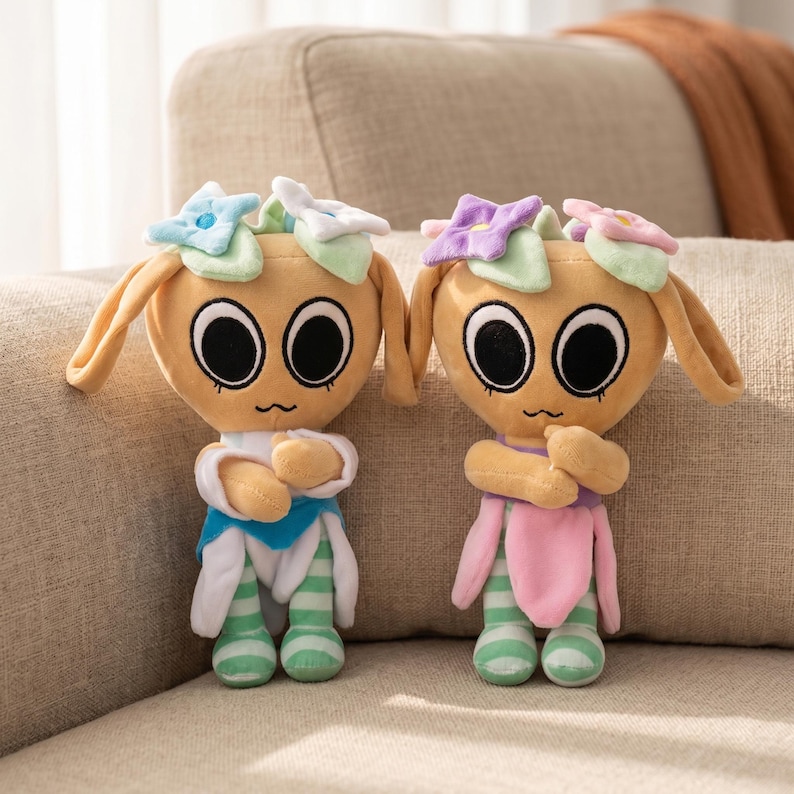 May include: Two plush dolls with large black eyes, tan bodies, and flower-shaped headbands. One doll wears a blue and white outfit, the other a pink and green outfit. Both have green and white striped legs and are posed on a beige couch.
