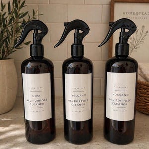 May include: Three amber glass spray bottles with black plastic triggers. Each bottle features a white rectangular label with black text reading Homestead, the scent name Diva or Volcano, All Purpose Cleaner, and Apothecary.