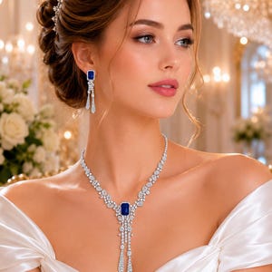 Può includere: Un set di gioielli composto da una collana e orecchini pendenti. La collana presenta una pietra preziosa blu rettangolare centrale circondata da piccole pietre chiare, con un design pendente a più fili. Gli orecchini sono abbinati.