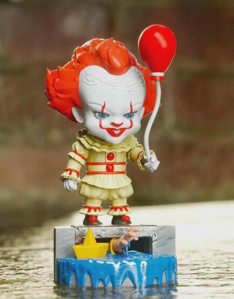 May include: A stylized vinyl figure of a clown with bright orange hair, white face paint, and red facial markings, wearing a cream-colored ruffled outfit with red buttons. The figure holds a red balloon and stands on a base featuring a sewer drain, a yellow paper boat, and a hand reaching out from blue water.