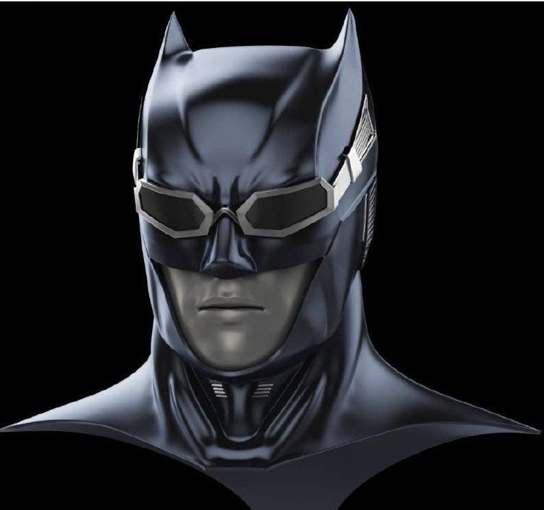 May include: A dark blue, smooth-textured cowl mask featuring pointed ears and integrated silver-rimmed goggles with dark lenses. The mask covers the head and neck, revealing a neutral-toned face with a defined nose, mouth, and chin area.