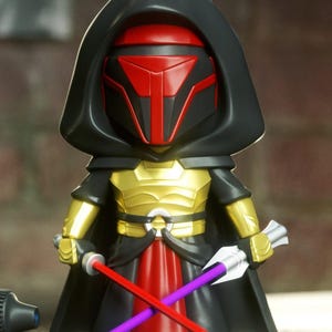May include: A stylized figurine of a character wearing a black hooded cloak, a red and black mask, and gold chest armor. The figure holds a red lightsaber in one hand and a purple lightsaber in the other, with a red fabric-like skirt piece.