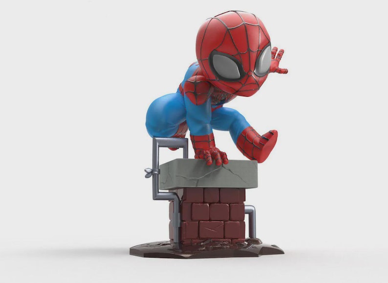 May include: A stylized figurine of a superhero character with a large head, wearing a red and blue suit with a black web pattern. The character is crouched on top of a brown brick chimney with a gray top, featuring a small gray pipe attached to the side.