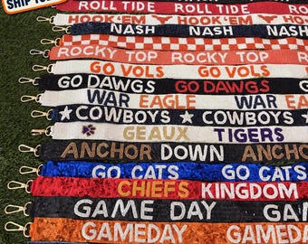 May include: A collection of beaded bag straps featuring various sports team slogans and colors, including text like GO GATORS, ROLL TIDE, HOOK EM, ROCKY TOP, GO VOLS, GO DAWGS, WAR EAGLE, COWBOYS, GEAUX TIGERS, ANCHOR DOWN, GO CATS, CHIEFS KINGDOM, GAME DAY, and TITAN UP.