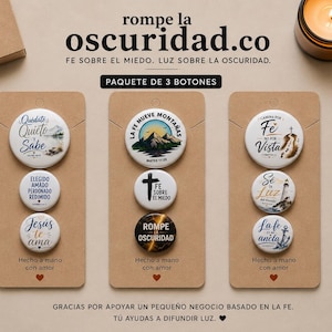 May include: Three sets of button pins with religious themes, each set on a brown card. The pins feature phrases like "Jesus te ama" and "Fe sobre el miedo." The background includes a candle and text that reads "rompe la oscuridad.co."