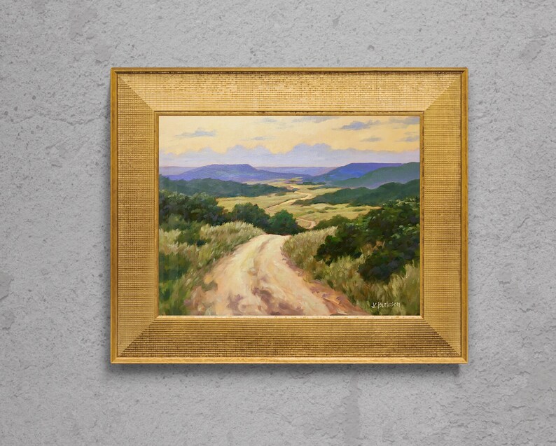 May include: An oil painting depicting a dirt track through a valley, set in a gold-coloured ornate frame. The landscape shows green trees, rolling hills, and a blue sky with clouds. The artist's signature is visible in the lower right corner.