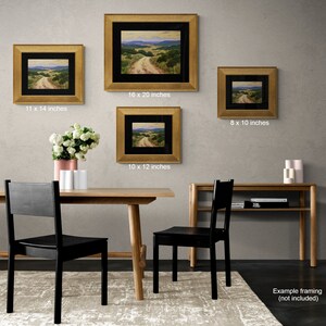 May include: Four framed landscape paintings with gold frames of varying sizes: 20.3 x 25.4 cm, 25.4 x 30.5 cm, 27.9 x 35.6 cm, and 40.6 x 50.8 cm. The paintings depict a dirt road winding through a valley with green hills and a blue sky. The paintings are displayed on a gray wall.