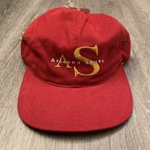 May include: A red baseball cap with a curved peak. The cap has gold embroidered "AS" lettering, with "Arizona State" in white below. The cap is structured and has a tag attached.