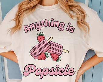 May include: A white t-shirt with the text "Anything is Popsicle" in pink lettering. The design features two pink popsicles with a strawberry on top of each.