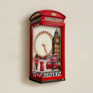 May include: A red telephone box souvenir with a London theme. It displays the London Eye, Big Ben, a double-decker bus, and the text "I ❤️ LONDON". The top of the booth has the word "TELEPHONE".