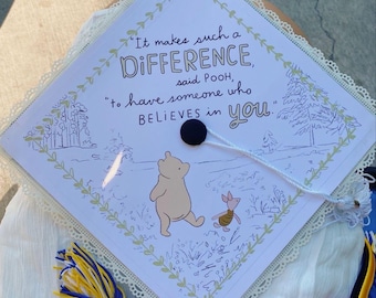 May include: A graduation cap with a Winnie the Pooh theme. The cap features a quote: "It makes such a DIFFERENCE, said POOH, to have someone who BELIEVES in you." The design includes illustrations of Winnie the Pooh and Piglet, with a tassel.