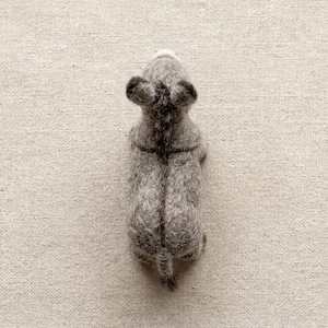 May include: A needle-felted gray donkey figurine viewed from directly above. The figure features a textured, fuzzy wool surface, two upright ears, a dark mane running down the center of the back, and a small tail extending from the rear end.