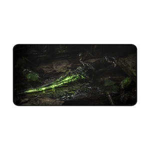 May include: A black rectangular mousepad featuring a glowing green dagger. The dagger is the focal point, emitting a bright, ethereal light against a dark, textured background. The overall theme is fantasy and weaponry.