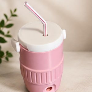 May include: A pink and white insulated tumbler with a lid and a straw. The tumbler has a cylindrical shape with vertical grooves and a white lid. The straw is white with red stripes.