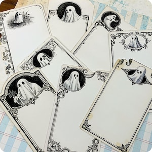 May include: A collection of rectangular paper cards featuring black and white illustrations of ghosts. Each card displays ornate decorative borders and circular frames containing ghost figures. The cards have varying shapes, including rounded corners and notched edges, with some showing aged, off-white paper tones.