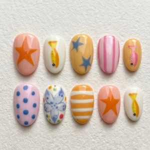 May include: A set of ten artificial nails with various designs. The nails feature a range of colors, including pink, orange, yellow, and white. Designs include stars, stripes, polka dots, and floral patterns. Each nail is oval-shaped.