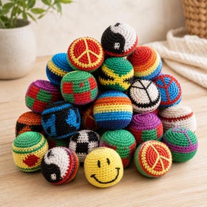 Puede incluir: Una colección de coloridas pelotas de malabares hechas a mano con ganchillo. Cada pelota presenta diseños únicos, incluyendo símbolos de la paz, símbolos del yin-yang, caras sonrientes y patrones geométricos. Las pelotas son de varios colores.