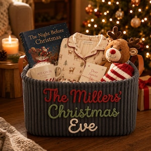 Könnte beinhalten: Ein dunkelgrauer Kord-Aufbewahrungskorb mit dem gestickten Text The Millers Christmas Eve, der ein Buch mit dem Titel The Night Before Christmas, eine weiße Tasse mit der Aufschrift Hot Cocoa, einen Schlafanzug mit Hirschmuster, ein Plüschrentier und eine Karte enthält.