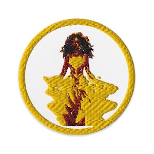 May include: Embroidered patch featuring a stylized figure in a yellow dress with red accents and black hair, set against a white background. The patch has a yellow border, creating a circular design. Ideal for jackets, bags, or other fabric items.