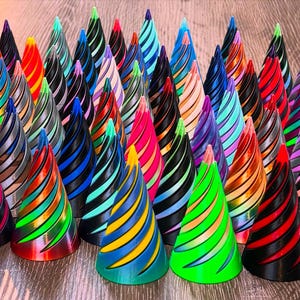 May include: A collection of colorful, cone-shaped decorative objects. Each cone features a black base with spiraling stripes in various colors, including red, green, blue, and yellow. The objects are arranged on a wooden surface.