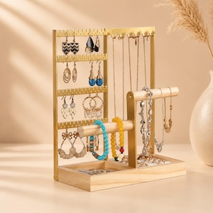 May include: A jewelry organizer stand featuring a gold-toned metal frame with multiple hooks for earrings and necklaces, paired with a light-colored wooden base and a horizontal wooden bar for bracelets, displaying various pieces of jewelry.