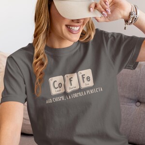 Peut inclure: T-shirt gris fonc&eacute; avec le mot "COFFEE" &eacute;pel&eacute; avec des &eacute;l&eacute;ments du tableau p&eacute;riodique. Le t-shirt porte &eacute;galement l'inscription "AND CHISME, LA FORMULA PERFECTA" en dessous.